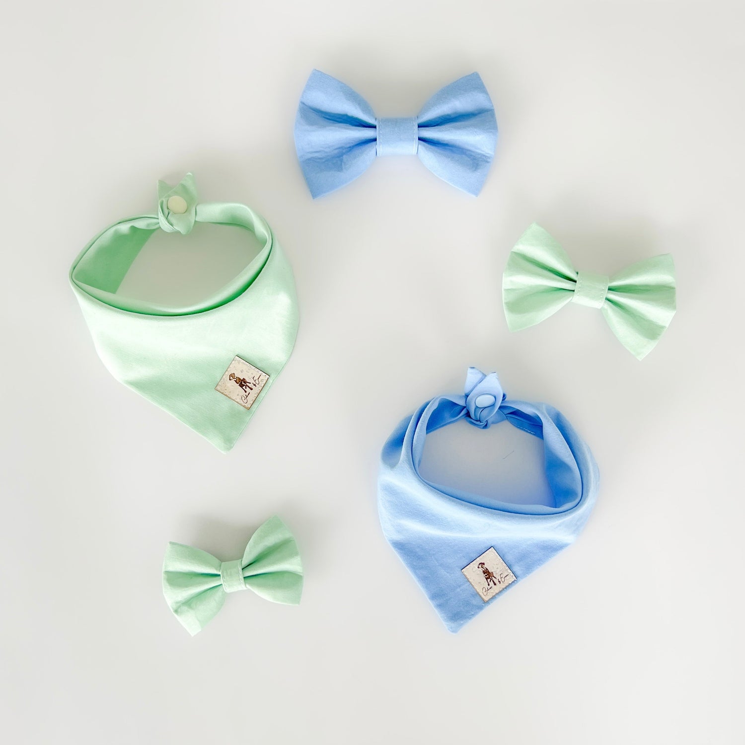 Pastel blue and mint green dog bandanas and dog bows by Colours By Emma laid out onto a white table