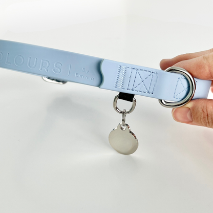 Light blue dog collar with a silver tag held by a hand on a white background